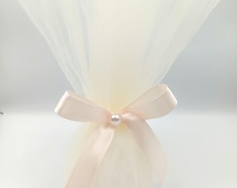 May include: A white tulle bag with a pink satin ribbon tied around it. A single pearl bead is in the center of the bow.