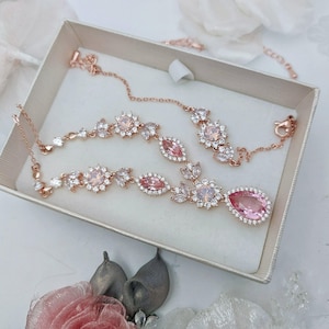 Op de afbeelding: Een set met een rose gouden ketting en armband met roze en heldere kristallen accenten. De ketting heeft een traanvormige hanger.