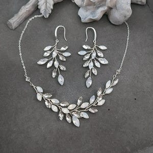 May include: A silver necklace and earrings set with a delicate branch design featuring clear and iridescent crystals.
