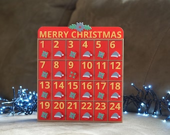 Puede incluir: Un calendario de adviento de madera rojo con las palabras "Merry Christmas" en la parte superior. El calendario tiene 24 puertas numeradas, cada una con una imagen diferente con temática navideña, incluyendo gorros de Papá Noel y acebo.