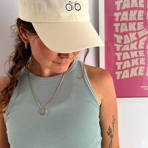 May include: Cream-colored baseball cap with a black bicycle graphic. The cap has a curved brim and a classic six-panel design. The hat is made of a soft, durable fabric.