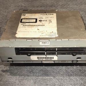 May include: A silver car stereo with a black faceplate and a slot for a CD. The stereo has the text "ALPINE" and "AL3200" printed on it. The stereo has a black slot for a CD and a black slot for a cassette tape.