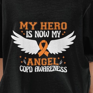 Puede incluir: Camiseta negra con el texto "MY HERO IS NOW MY ANGEL COPD AWARENESS". El diseño incluye alas de ángel blancas y una cinta naranja. El texto es en naranja y blanco.