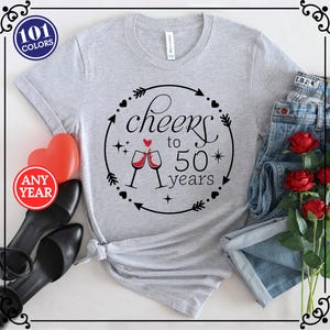 May include: Gray t-shirt with a black and white graphic design that says "Cheers to 50 years" with two wine glasses and a heart. The graphic is surrounded by arrows and hearts.