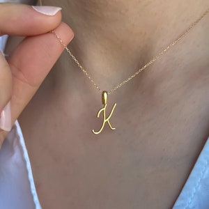 Può includere: Una collana con catena d'oro con un ciondolo a forma di lettera K corsiva.