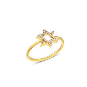 Peut inclure: Une bague en or ornée d'un motif en forme d'étoile à six branches centré sur l'anneau. L'étoile est incrustée de petites pierres claires et scintillantes qui recouvrent toute sa surface, créant un aspect brillant et réfléchissant sur le métal.
