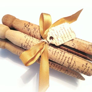 Puede incluir: Un paquete de pinzas de madera para la ropa atadas con una cinta dorada y una etiqueta que dice "Just a little something" en escritura cursiva.