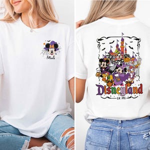 A woman wearing a white t-shirt with a graphic of Minnie Mouse and Disneyland on the back, as well as a graphic of a castle and bats on the front.