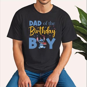 a man sitting on a stool wearing a shirt that says dad of the birthday boy