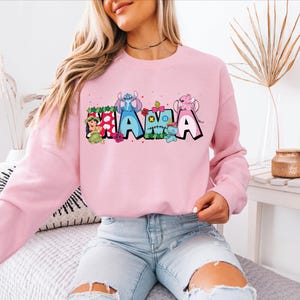 a woman sitting on a bed wearing a pink sweatshirt