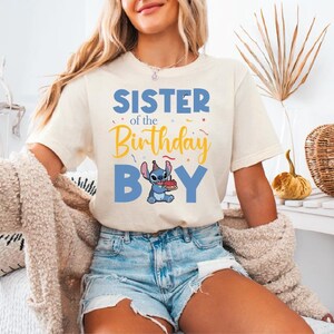 a woman sitting on a bed wearing a shirt that says sister of the birthday boy