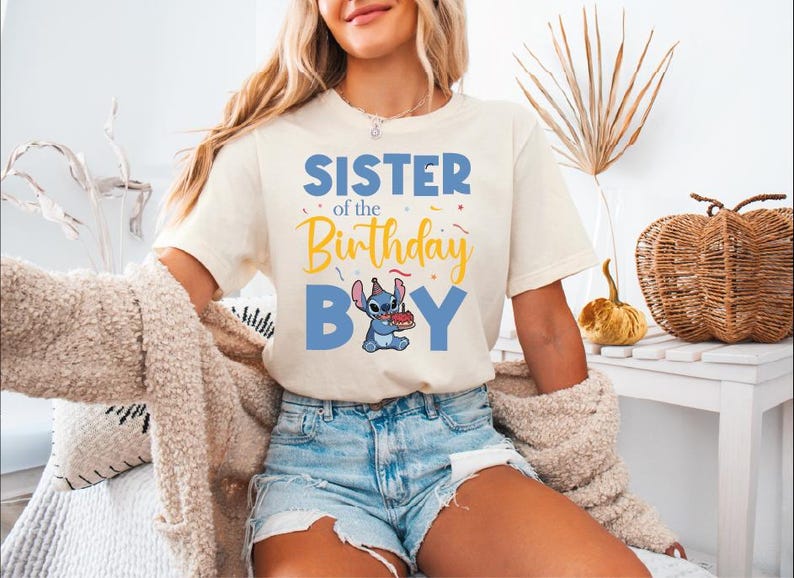 a woman sitting on a bed wearing a shirt that says sister of the birthday boy