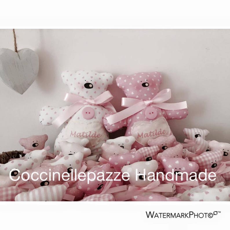 Puede incluir: Ositos de peluche hechos a mano en tela blanca y rosa, con dise&ntilde;os de corazones. Cada oso tiene una cinta rosa y un bot&oacute;n. El texto "Matilde" est&aacute; en el pecho del oso. La imagen incluye el texto "Coccinellepazze Handmade".