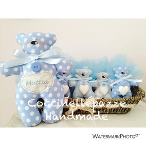 Puede incluir: Una colecci&oacute;n de osos de peluche hechos a mano, azules y blancos con lunares. El oso m&aacute;s grande tiene un lazo azul claro, un bot&oacute;n y un parche en forma de coraz&oacute;n con el nombre "Mattia". Los osos est&aacute;n en una cesta de mimbre.