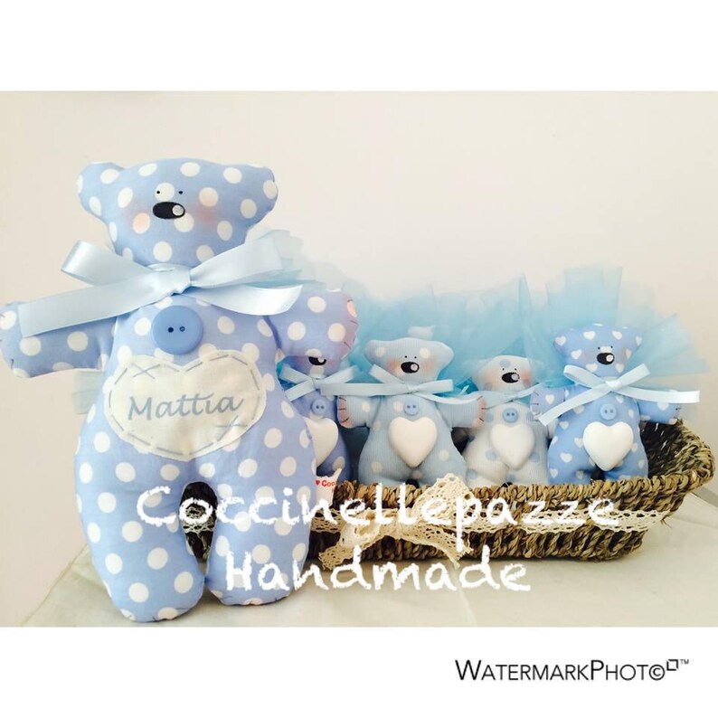 Puede incluir: Una colecci&oacute;n de osos de peluche hechos a mano, azules y blancos con lunares. El oso m&aacute;s grande tiene un lazo azul claro, un bot&oacute;n y un parche en forma de coraz&oacute;n con el nombre "Mattia". Los osos est&aacute;n en una cesta de mimbre.