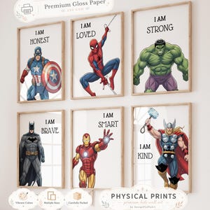 Op de afbeelding: Zes ingelijste prints met superheldenillustraties. Elke print toont een superheld en een positieve bevestiging: Eerlijk, Geliefd, Sterk, Dapper, Slim en Vriendelijk. De prints zijn gelabeld met "Premium Gloss Paper" en "Physical Prints".