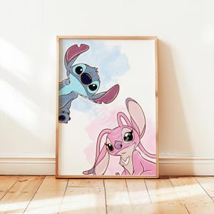 May include: A framed print featuring cartoon characters Stitch and Angel. Stitch is blue with large ears, and Angel is pink. The background has blue and pink watercolour-style washes. The frame is a light wood colour.