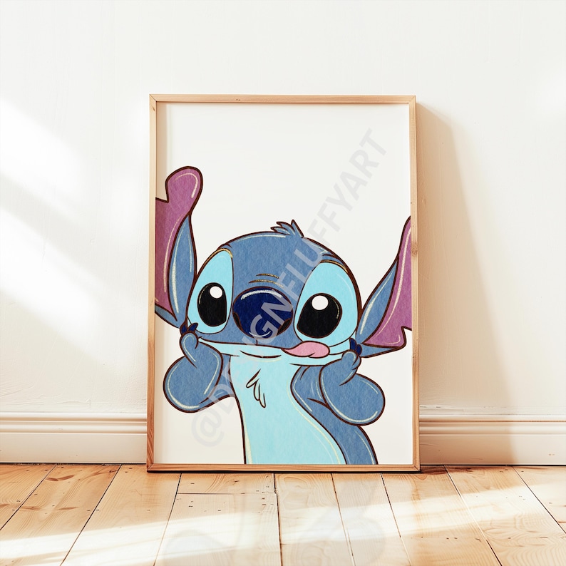 May include: A framed print featuring a cartoon character with blue fur, large black eyes, and pink ears. The character is smiling and sticking out its tongue, with its hands near its face. The artwork is set against a white background.