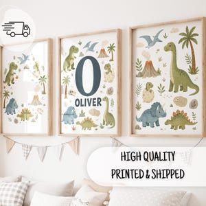 Op de afbeelding: Drie ingelijste wandposters met illustraties van diverse dinosaurussen, vulkanen en palmbomen. De middelste poster toont een grote letter O en de naam OLIVER. De kunstwerken gebruiken een kleurenpalet van groene, blauwe en bruine tinten.