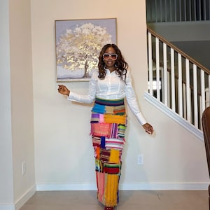 May include: A long, ankle-length skirt constructed from various rectangular patches of fabric in vibrant colors including yellow, orange, pink, blue, and purple, featuring raw, frayed edges and a white long-sleeved button-down shirt with a collar.