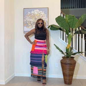Könnte beinhalten: Ein schwarzes ärmelloses Oberteil und ein langer, farbenfroher Rock. Der Rock hat horizontale Streifen in Rosa, Orange, Blau und Grün, mit einem Schlitz vorne und Fransen. Ein goldener Reißverschluss verläuft vorne. Der Rock ist etwa 100 cm lang.