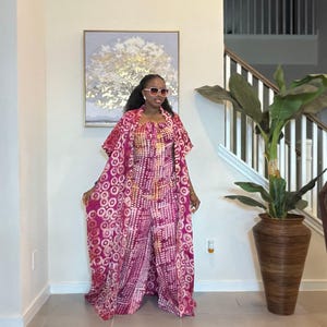 May include: A magenta and white patterned jumpsuit featuring a sleeveless bodice with a tie-front detail and wide-leg trousers, paired with a matching floor-length open-front duster kimono with a circular print and oversized square sunglasses.