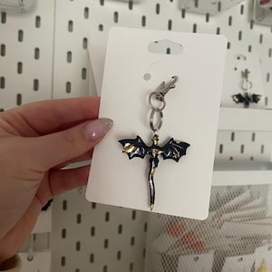 May include: Black and gold dragon keyring with a silver chain and clasp. The dragon is flying with its wings spread out.