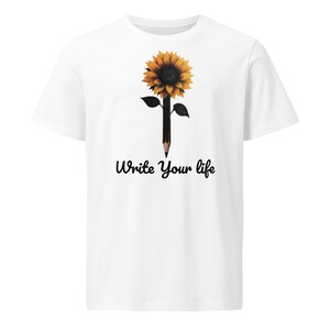 Può includere: Una t-shirt bianca a maniche corte con la grafica di un girasole giallo con il gambo a forma di matita nera e due foglie. Sotto la grafica, il testo "Write Your life" è stampato in un carattere corsivo nero al centro del capo.