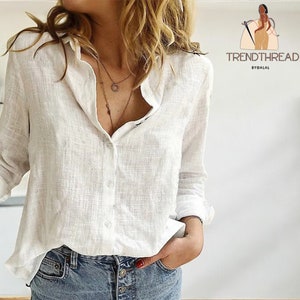 Könnte beinhalten: Ein weißes, langärmliges Hemd aus Leinen mit Knöpfen. Das Hemd ist leicht oversized und hat eine lockere Passform. Das Model trägt das Hemd zu einer blauen Jeans.