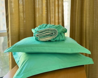 May include: Two mint green pillowcases stacked on top of a rolled up mint green fitted sheet. The sheet is folded in half and the pillowcases are folded in half. The items are sitting on a wooden surface.