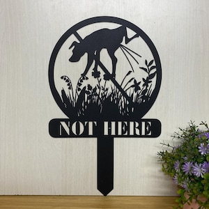 May include: Black metal garden sign with a silhouette of a dog pooping in a circle with a red slash through it. The sign says "NOT HERE" in white letters.