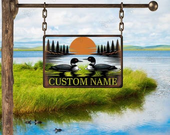 May include: A rectangular metal sign depicting a lake scene with two loons, a setting sun, and pine trees. The sign hangs from a chain and has the words "CUSTOM NAME" at the bottom. The sign is mounted on a wooden post.