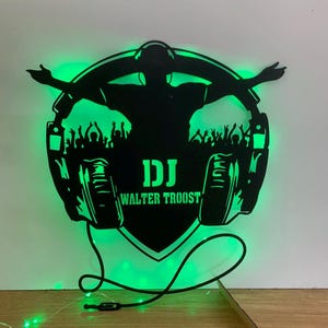 Könnte beinhalten: Schwarze Silhouette eines DJs mit Kopfhörern und einer Menschenmenge vor ihm. Die Silhouette wird mit grünen LED-Lichtern beleuchtet. Der Text "DJ WALTER TROOST" befindet sich auf der Silhouette.