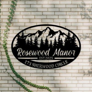 Peut inclure: Panneau ovale en métal noir avec une silhouette de chaîne de montagnes et des pins. Le panneau indique "Rosewood Manor Est. 2025 173 Sherwood Circle".
