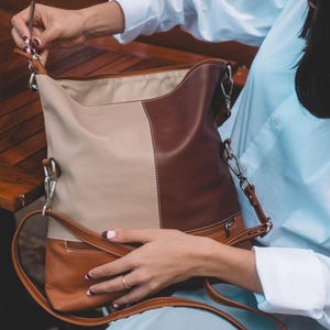 Close-up of hands opening a two-tone leather tote bag, highlighting its spacious interior.