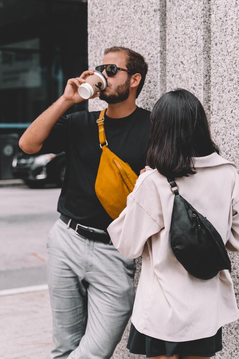 Man drinking coffee while wearing a mustard-yellow leather side bag crossbody. The casual and vibrant color choice makes this bag a unique fashion accessory.