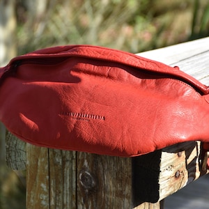 Close-up of a red leather fanny pack displayed outdoors on a wooden post, showcasing its sleek and bold design suitable for casual outings.