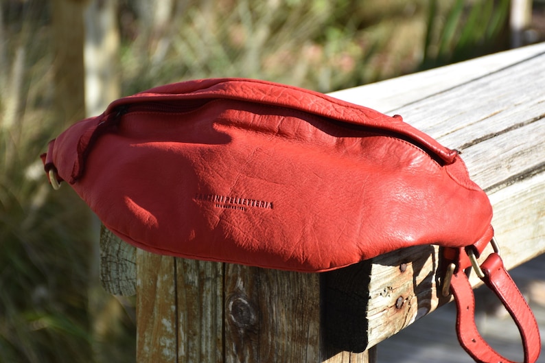 Close-up of a red leather fanny pack displayed outdoors on a wooden post, showcasing its sleek and bold design suitable for casual outings.