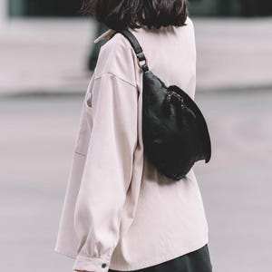 Close-up of a woman wearing a black leather belt bag crossbody over a light beige oversized shirt. The belt bag adds a minimalist yet chic touch, ideal for everyday style.