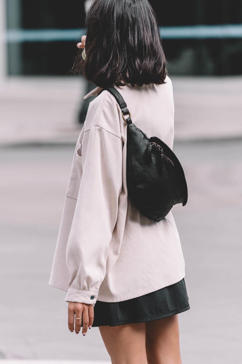 Close-up of a woman wearing a black leather belt bag crossbody over a light beige oversized shirt. The belt bag adds a minimalist yet chic touch, ideal for everyday style.