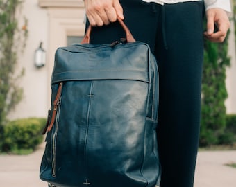 May include: A dark blue leather backpack with brown leather accents and gold hardware. The backpack has a zippered front pocket and a large main compartment.