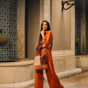 Woman standing against a stone building, wearing an orange outfit and carrying the chic leather tote bag over her shoulder.