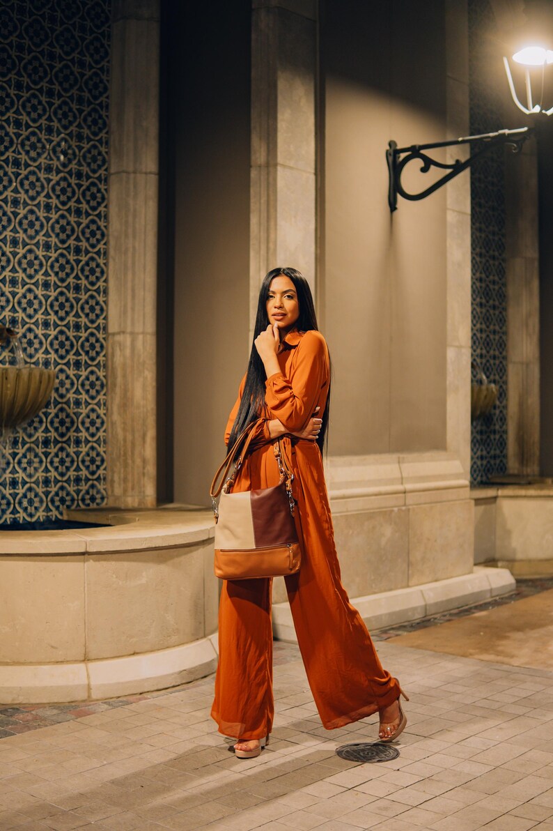 Woman standing against a stone building, wearing an orange outfit and carrying the chic leather tote bag over her shoulder.