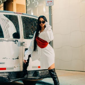 Woman in white shirt wearing a red leather hip bag. A trendy, modern crossbody bag that combines luxury leather with practicality. This stylish fanny pack is perfect for festivals, travel, or everyday carry.