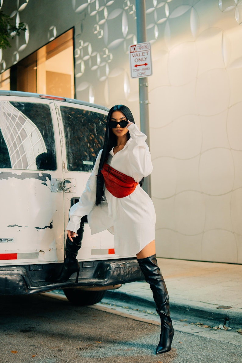 Woman in white shirt wearing a red leather hip bag. A trendy, modern crossbody bag that combines luxury leather with practicality. This stylish fanny pack is perfect for festivals, travel, or everyday carry.
