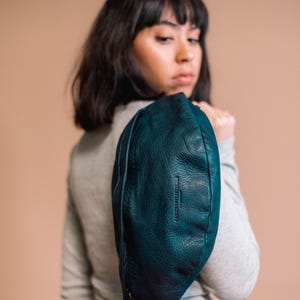 Woman wearing a chic dark blue leather belt bag over her shoulder, showcasing its smooth texture and high-quality craftsmanship. Ideal as a fanny pack, bum bag, or side bag for a stylish, hands-free accessory.