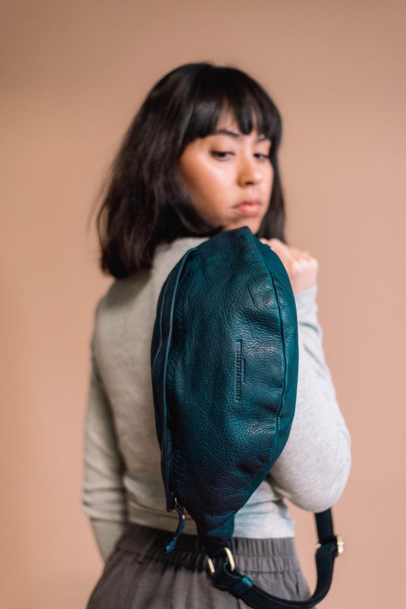 Woman wearing a chic dark blue leather belt bag over her shoulder, showcasing its smooth texture and high-quality craftsmanship. Ideal as a fanny pack, bum bag, or side bag for a stylish, hands-free accessory.