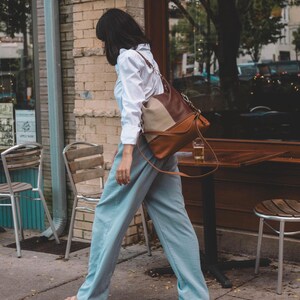 Woman walking by a cafe, carrying a stylish two-tone leather tote over her shoulder