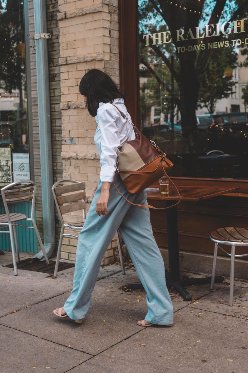 Woman walking by a cafe, carrying a stylish two-tone leather tote over her shoulder