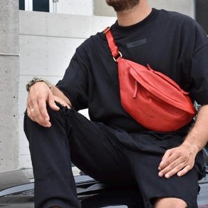 Man wearing a red leather fanny pack over a black outfit. This stylish crossbody bag is a perfect blend of trend and functionality, ideal for everyday use or festivals. A modern, high-quality leather bag for carrying essentials